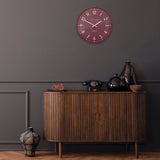 A simple and modern round wall clock in a berry colour with gold hands and numbers on wall