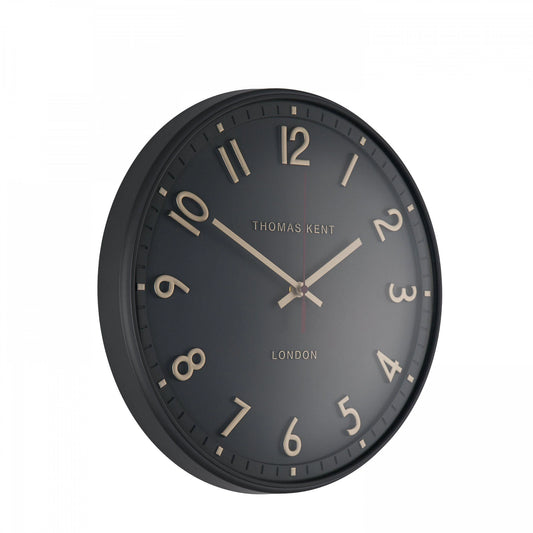 A simple and modern round wall clock in a charcoal colour with gold hands and numbers side view