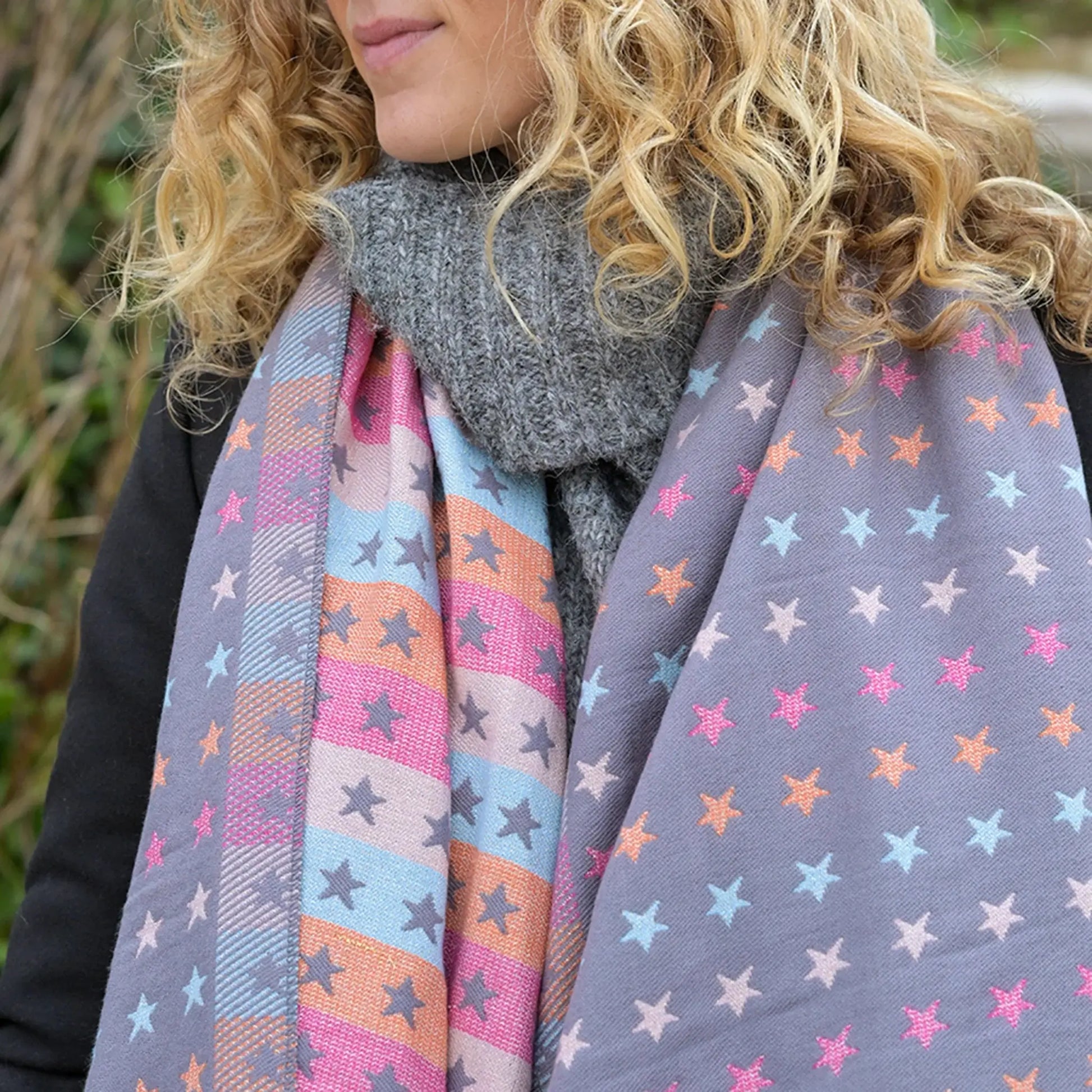 Model wearing reversible grey and pastel rainbow stars and stripes scarf