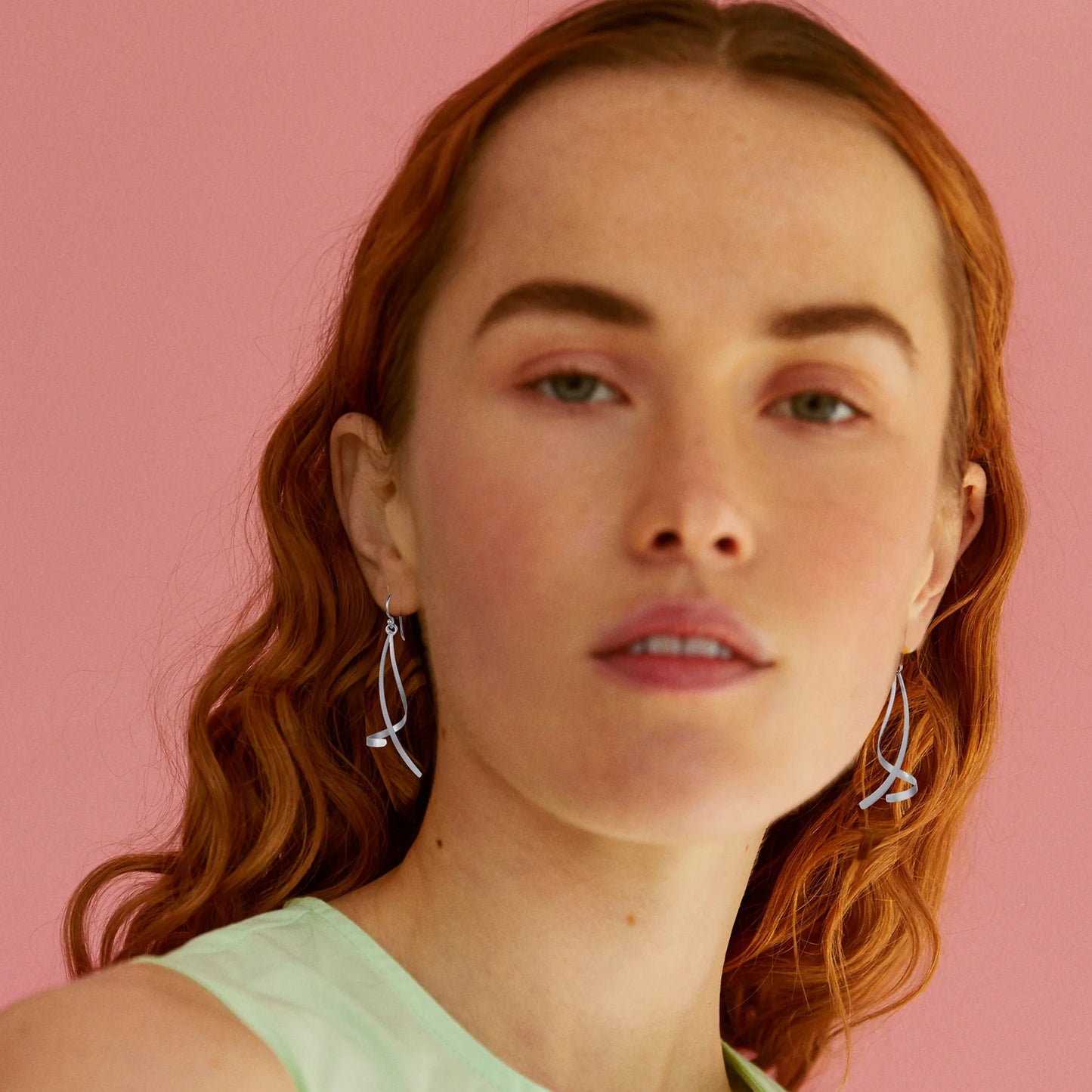 Model wearing satin silver dangling earrings with two ribbon twist shapes