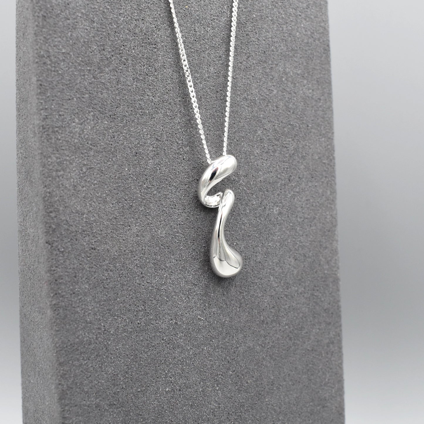 A sterling silver pendant that features a modern design of a long twisted droplet shape