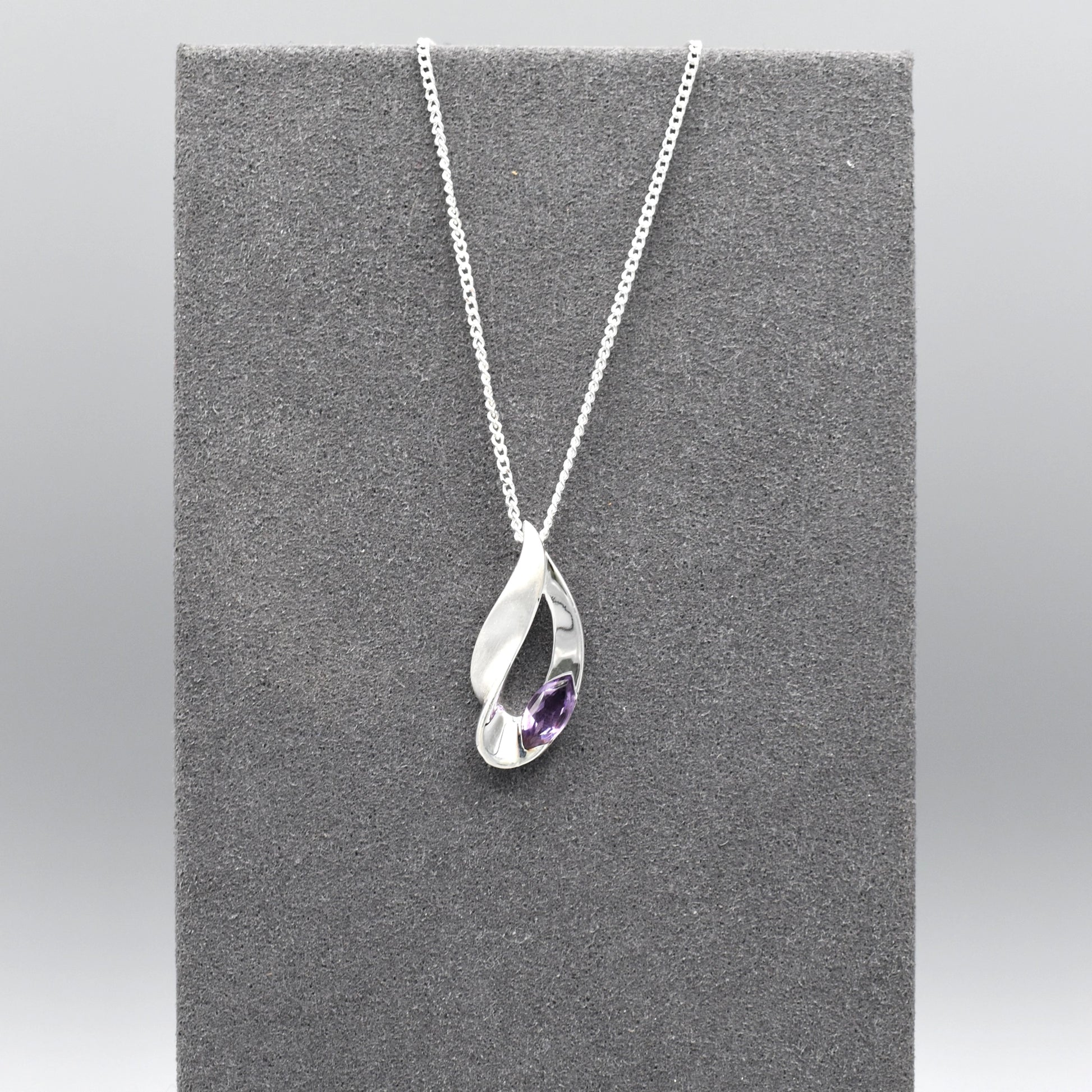 A silver pendant featuring a twisted marquis shape with a marquis cut amethyst stone