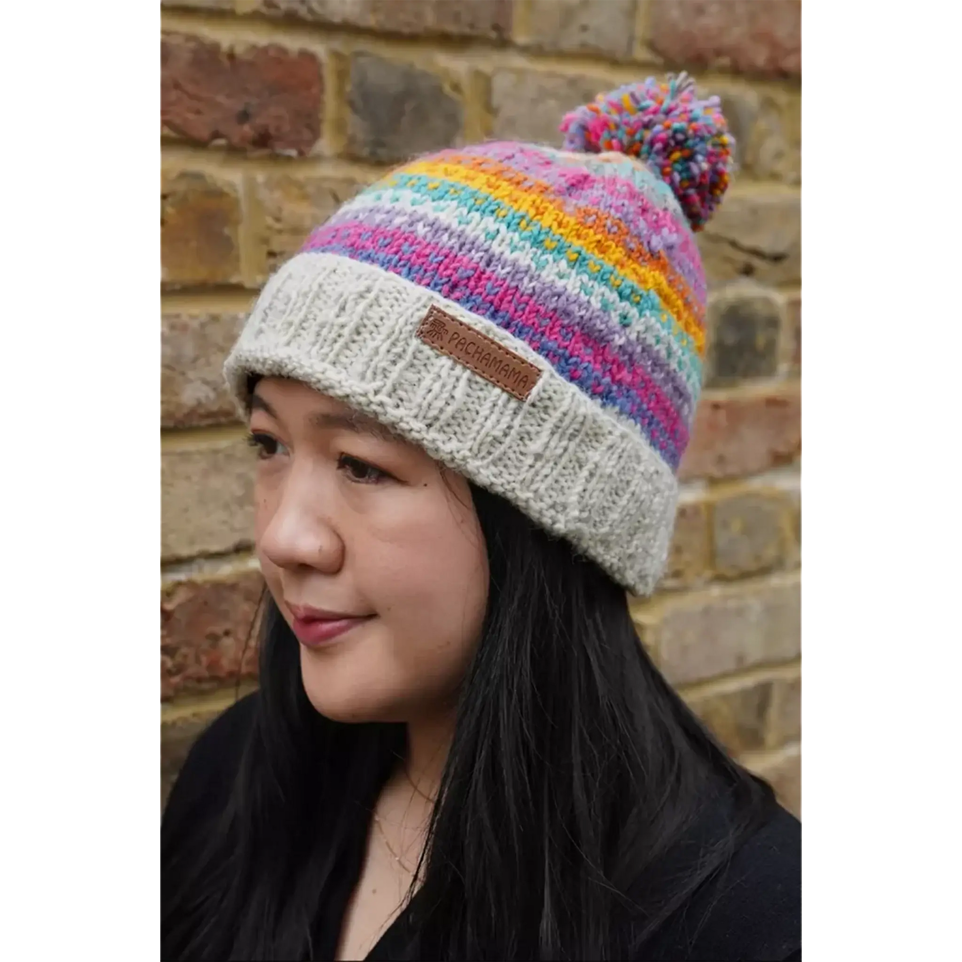 Model wearing a bobble beanie hat with rainbow stripes and hearts