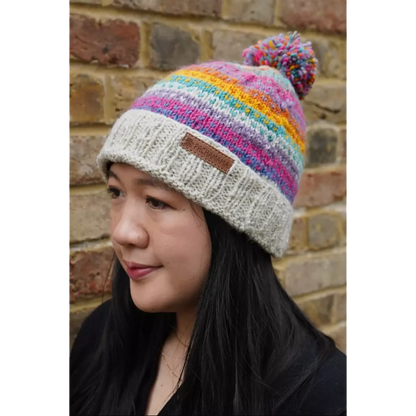 Model wearing a bobble beanie hat with rainbow stripes and hearts