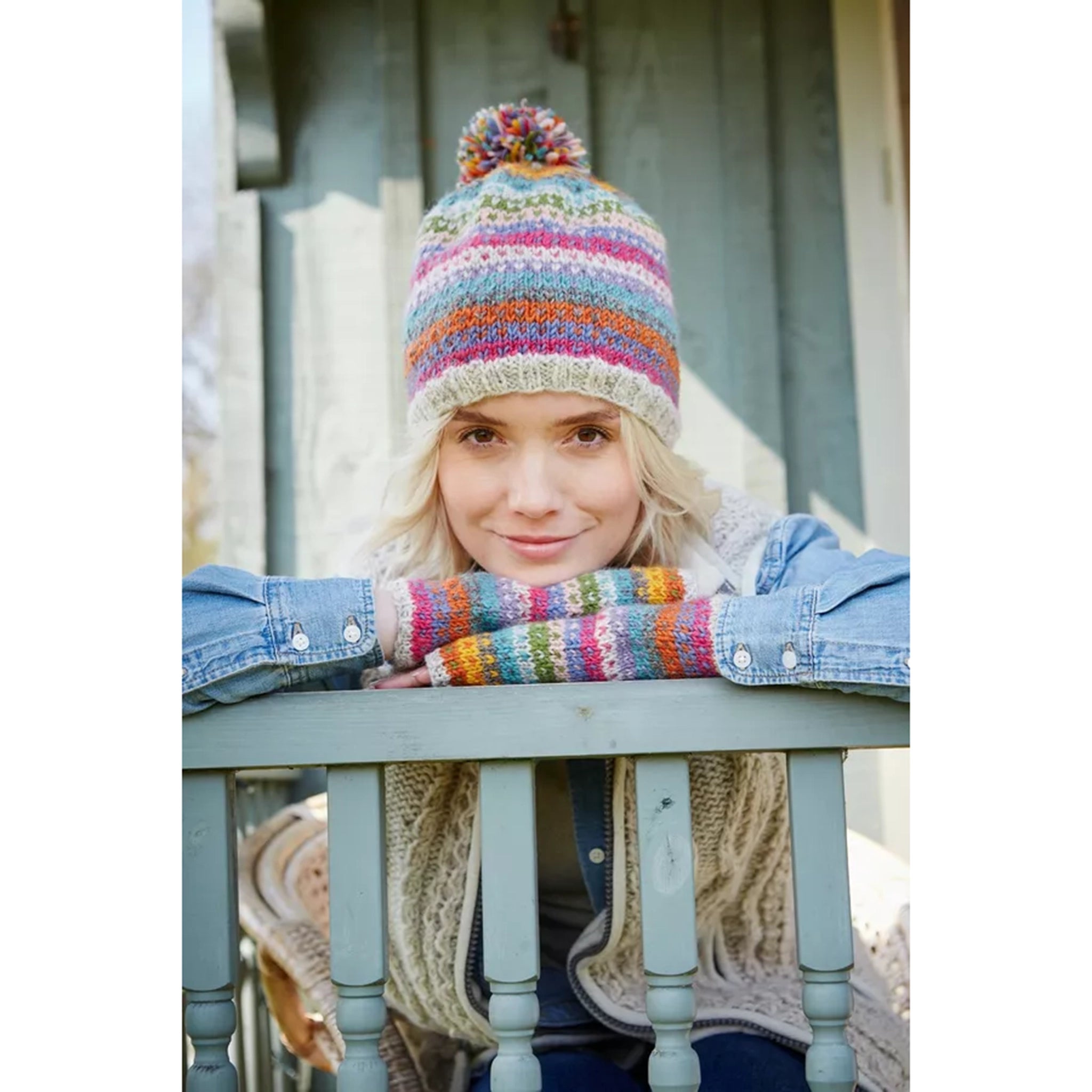 Model wearing a pastel multicolour striped knitted pompom hat with little chevron hearts