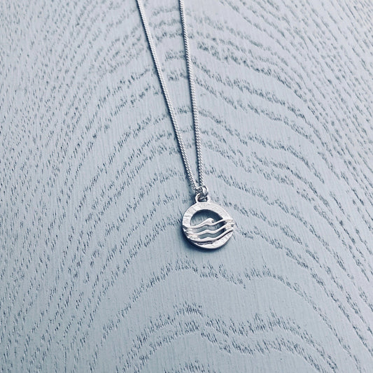 A silver pendant featuring a simple round textured frame overlaid with three waves 