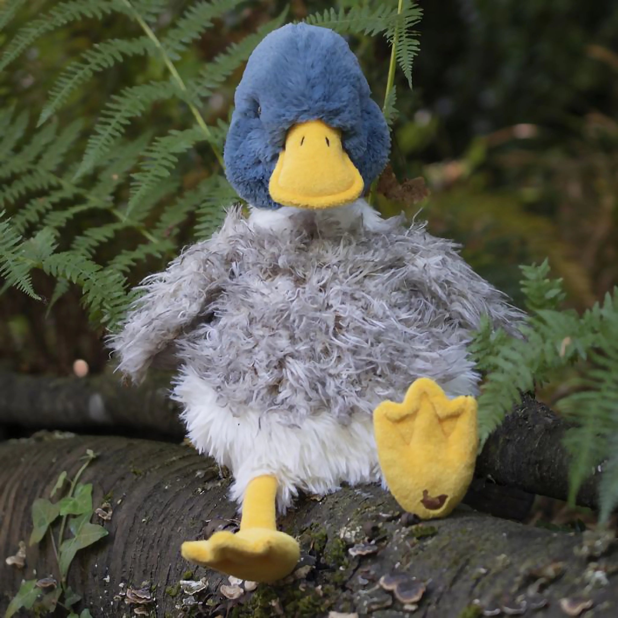 A stuffed duck plush toy with the Wrendale logo embroidered on the bottom of its foot posed on a branch