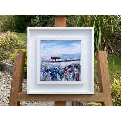 A ceramic tile printed with an abstract painting of a cottage and flowers mounted on a white frame