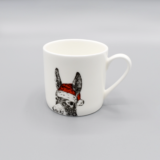 A white china espresso mug featuring a print of a donkey wearing a bright red Santa hat