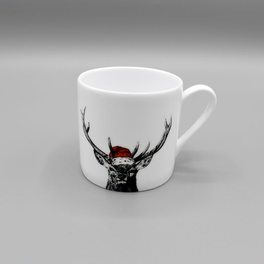 A white china espresso mug featuring a print of a stag wearing a red Santa hat