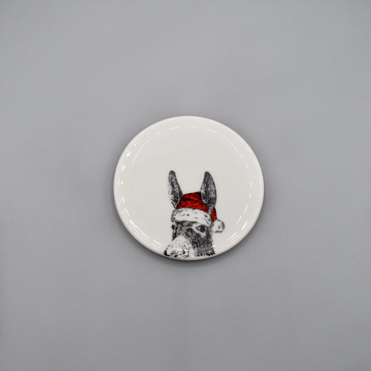A white china coaster featuring a print of a donkey with a bright red Santa hat