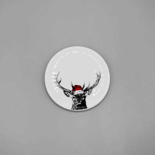 A white china coaster featuring a print of a stag with a bright red Santa hat
