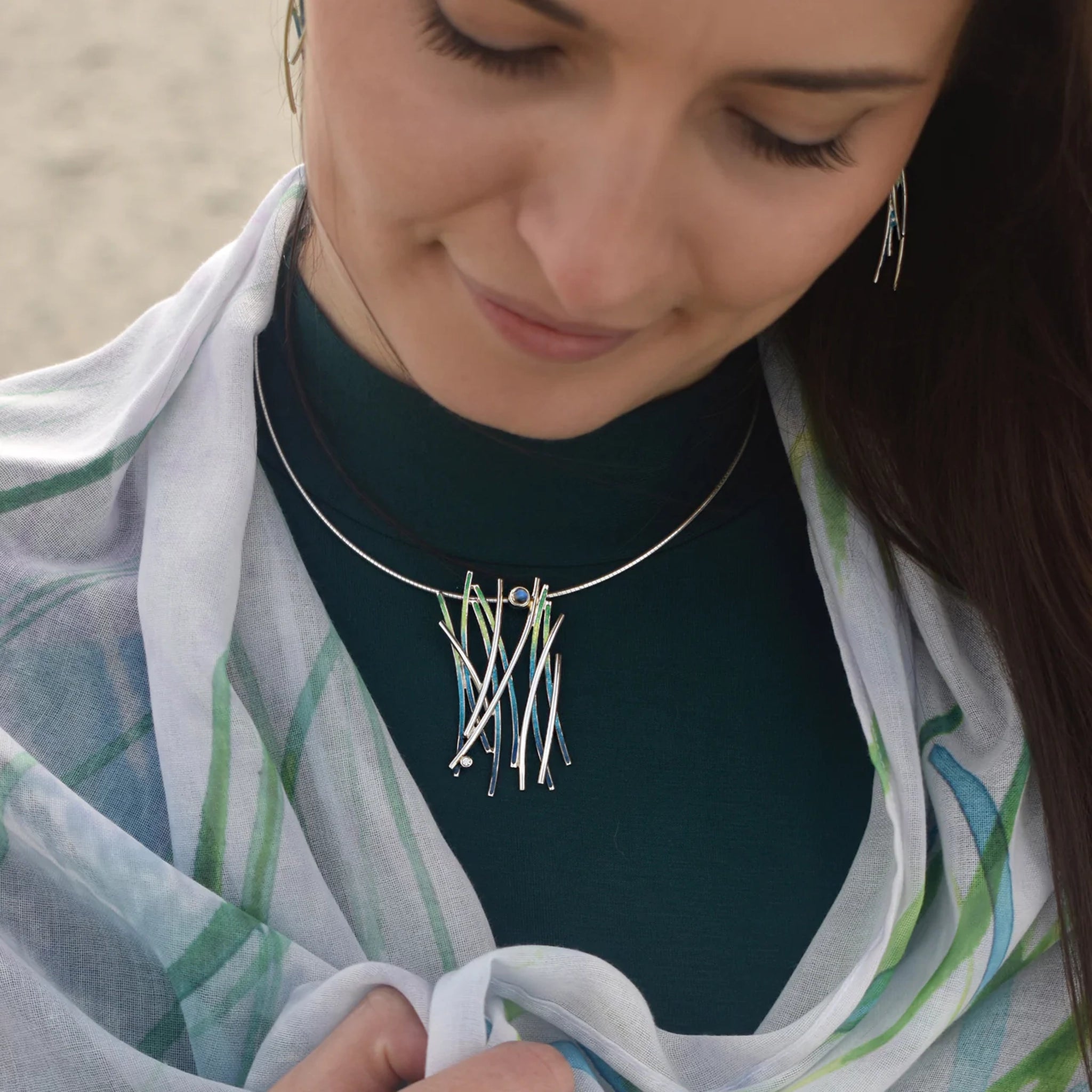 Model wearing necklet in silver and green/blue enamel with a moonstone and cubic zirconia on neck wire