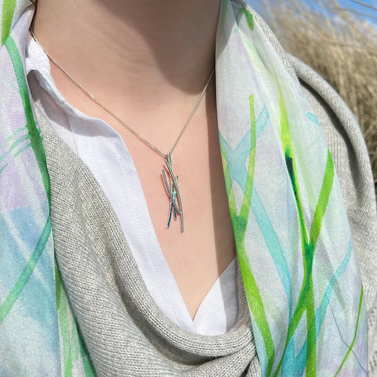 Model wearing silver pendant with four strands, two silver and two in green and blue enamel on silver chain