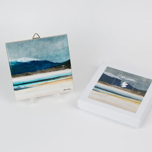 A ceramic tile featuring a seaside scene painting by Cath Waters with packaging