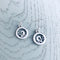 A pair of silver earrings featuring round frames with curled waves in the centre