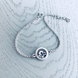 A silver chain bracelet featuring a round pendant with a frame and curled wave design