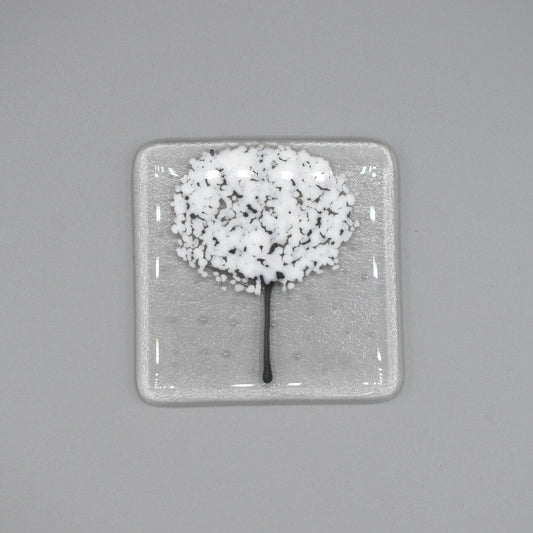 A clear glass square coaster with a white tree design