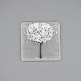 A clear glass square coaster with a white tree design