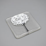 A clear glass square coaster with a white tree design side 