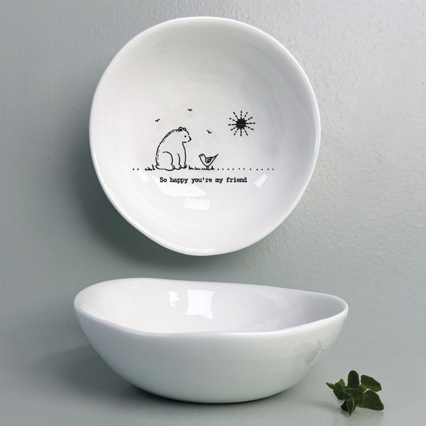 A white ceramic bowl featuring a bird and bear illustration and a quote