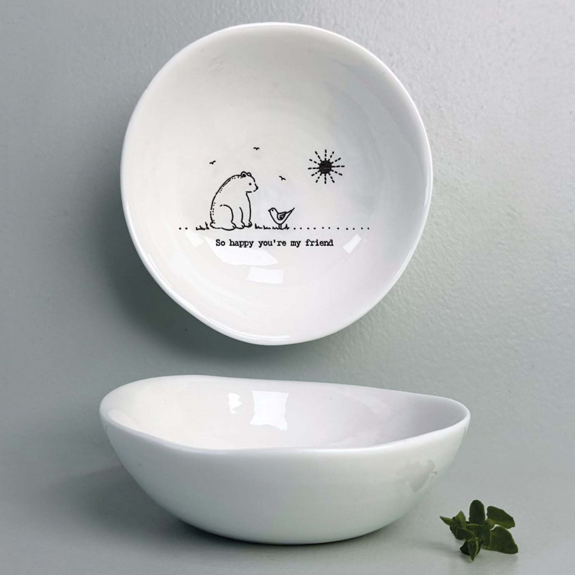 A white ceramic bowl featuring a bird and bear illustration and a quote
