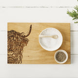 Wooden cutting board with engraved Highland cow staged with salt and pepper bowls