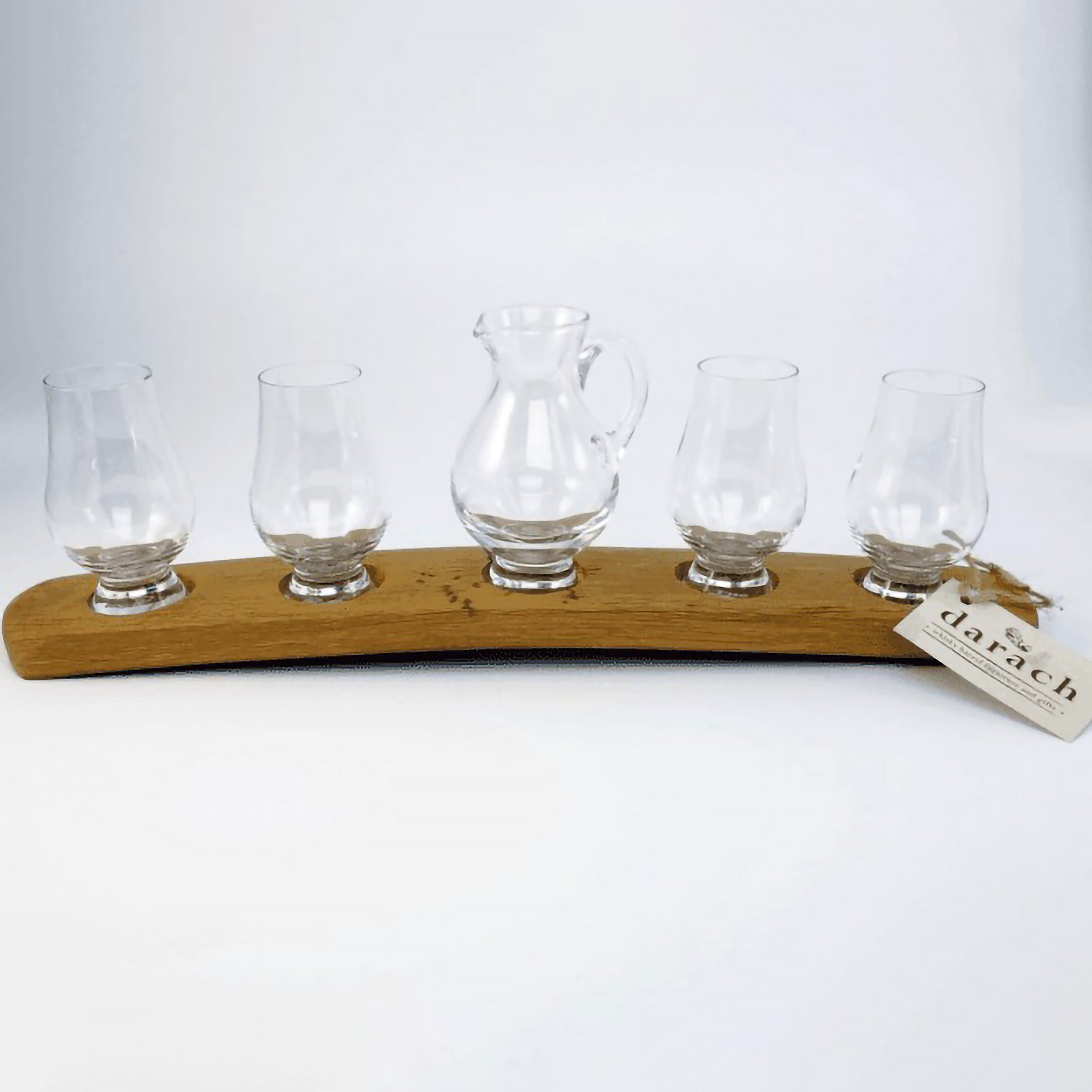 Four nosing whisky glasses and single glass jug on wooden barrel stave