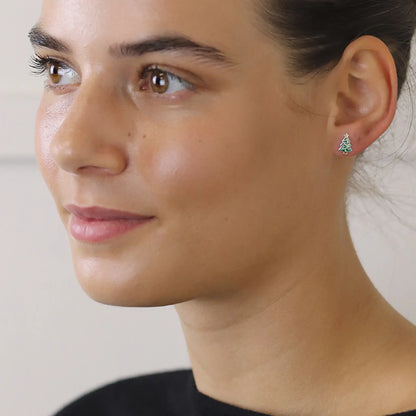 Model wearing pair of silver stud earrings shaped like Christmas trees with enamelled details