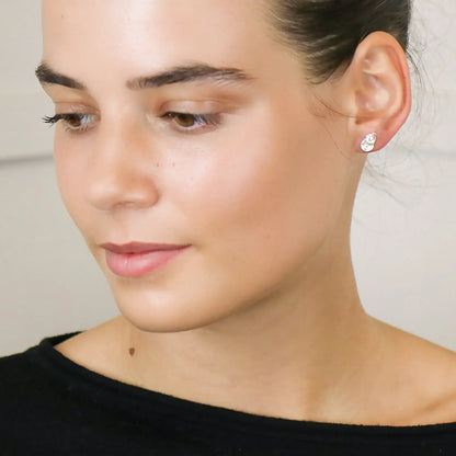 Model wearing a pair of silver stud earrings shaped like snowmen with enamelled details