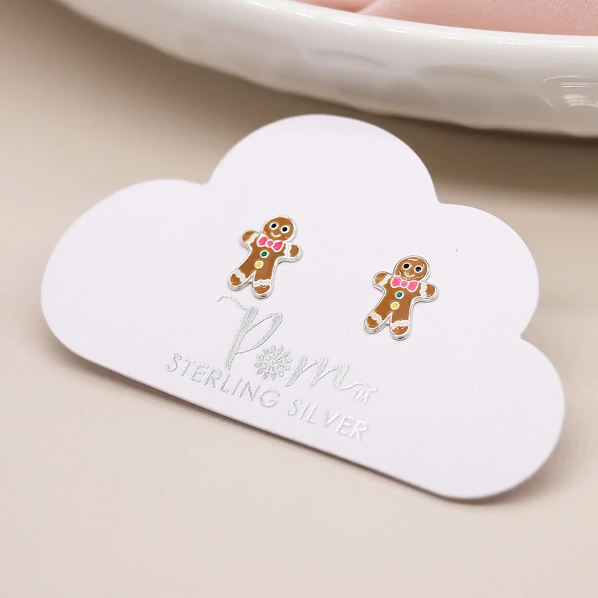 Pair of silver stud earrings shaped like gingerbread men with enamelled details on card