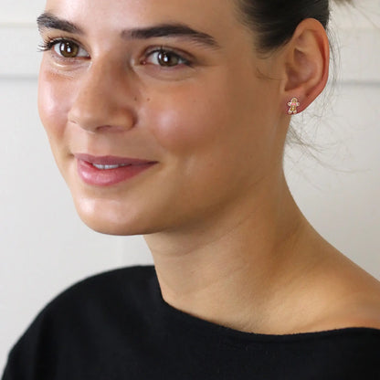 Model wearing a pair of silver stud earrings shaped like gingerbread men with enamelled details