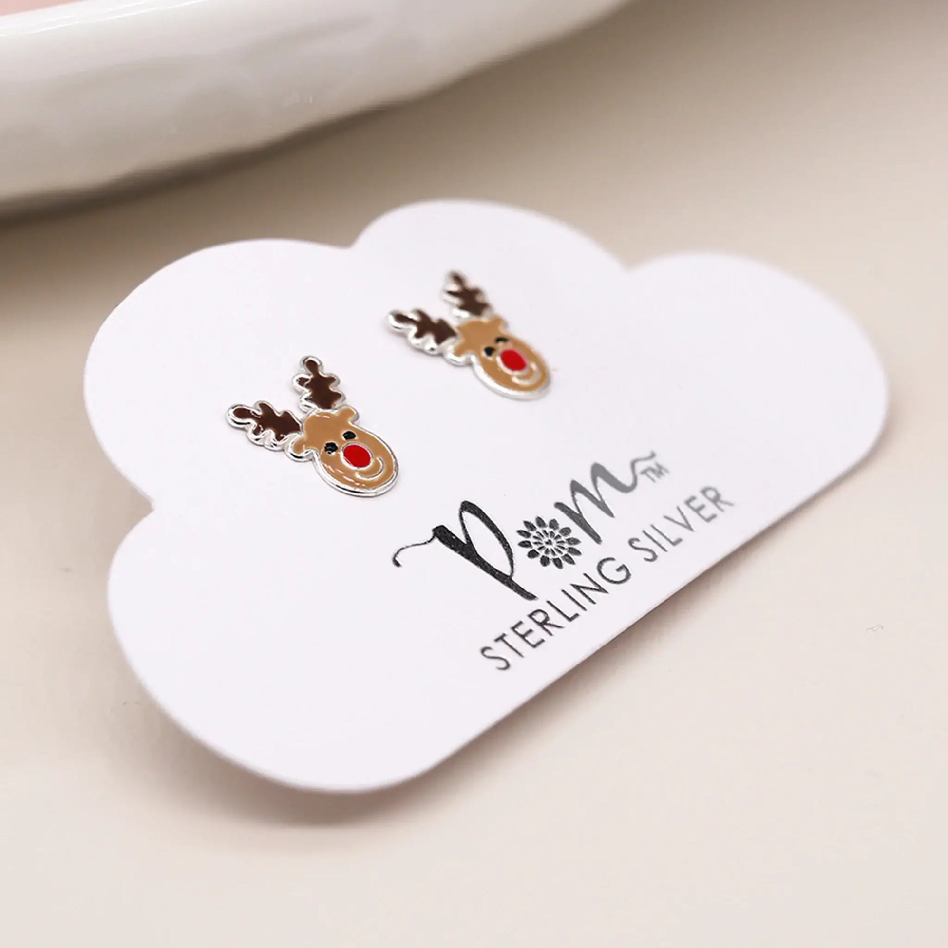 Pair of silver stud earrings shaped like Rudolph the reindeer with enamelled details on packaging card
