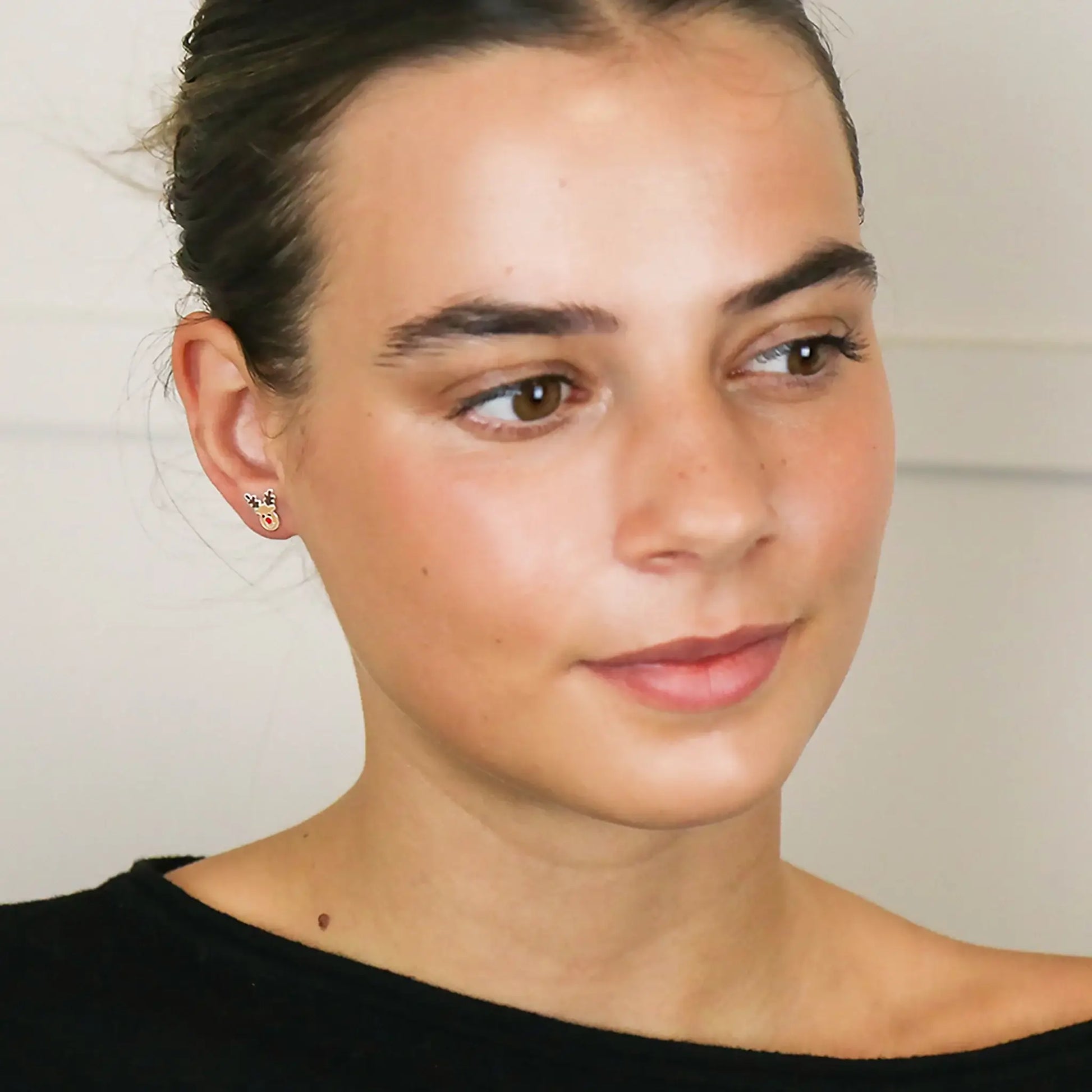 Model wearing a pair of silver stud earrings shaped like Rudolph the reindeer with enamelled details