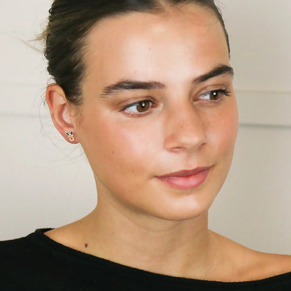 Model wearing a pair of silver stud earrings shaped like Rudolph the reindeer with enamelled details