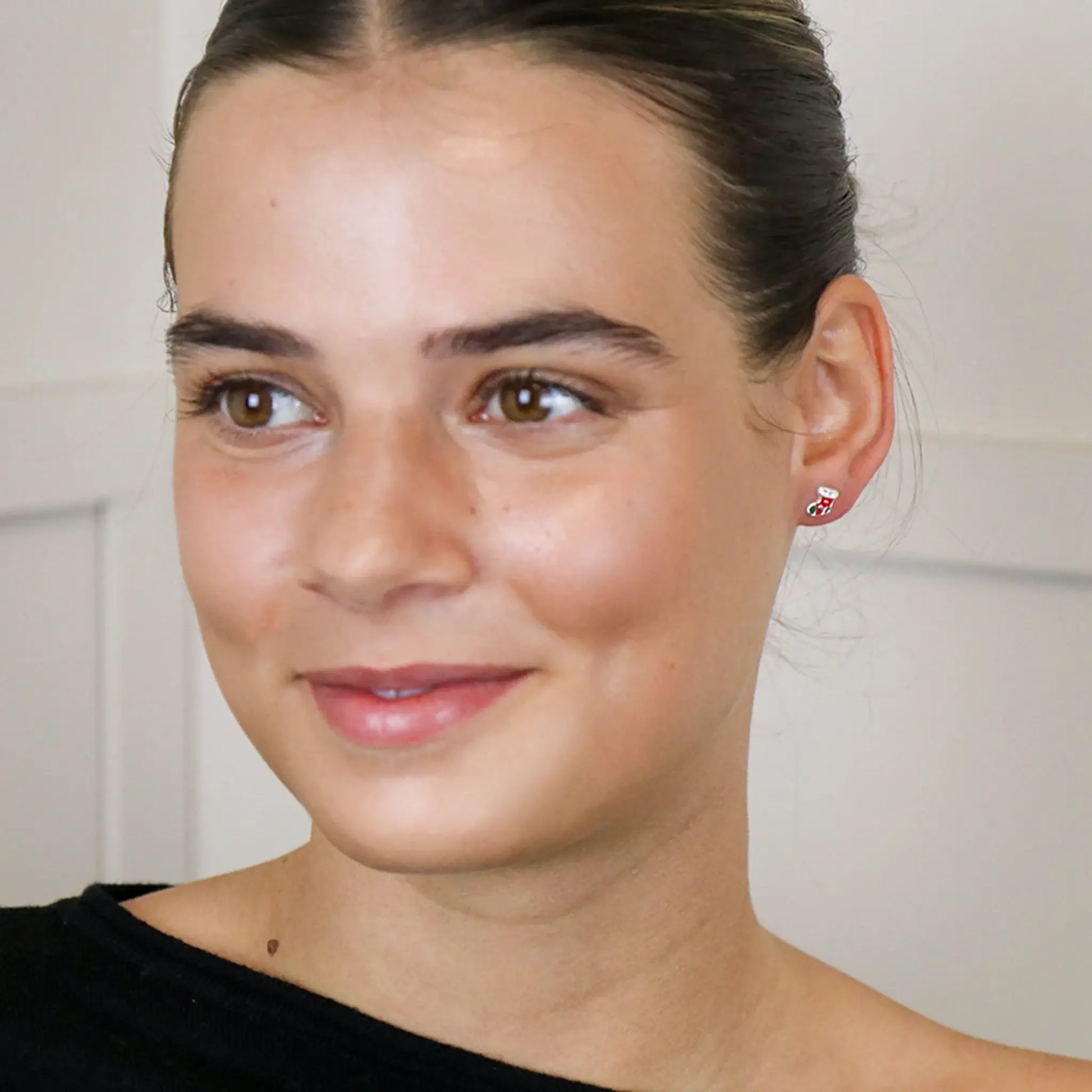 Model wearing a pair of silver stud earrings shaped like stockings with enamelled details