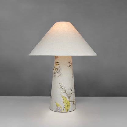 A fabric table lamp with shade and a yellow blossom design on the conical base lit up