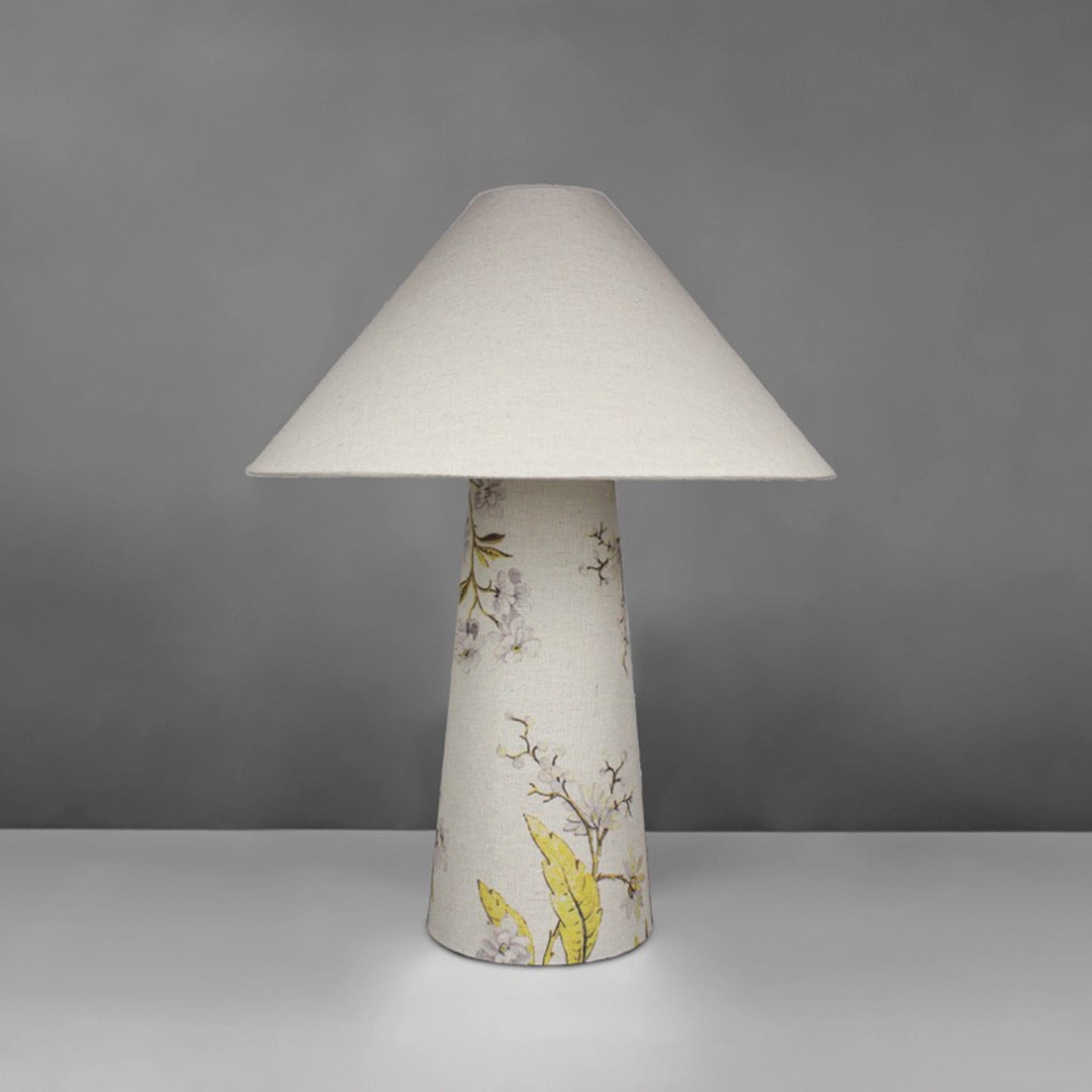A fabric table lamp with shade and a yellow blossom design on the conical base