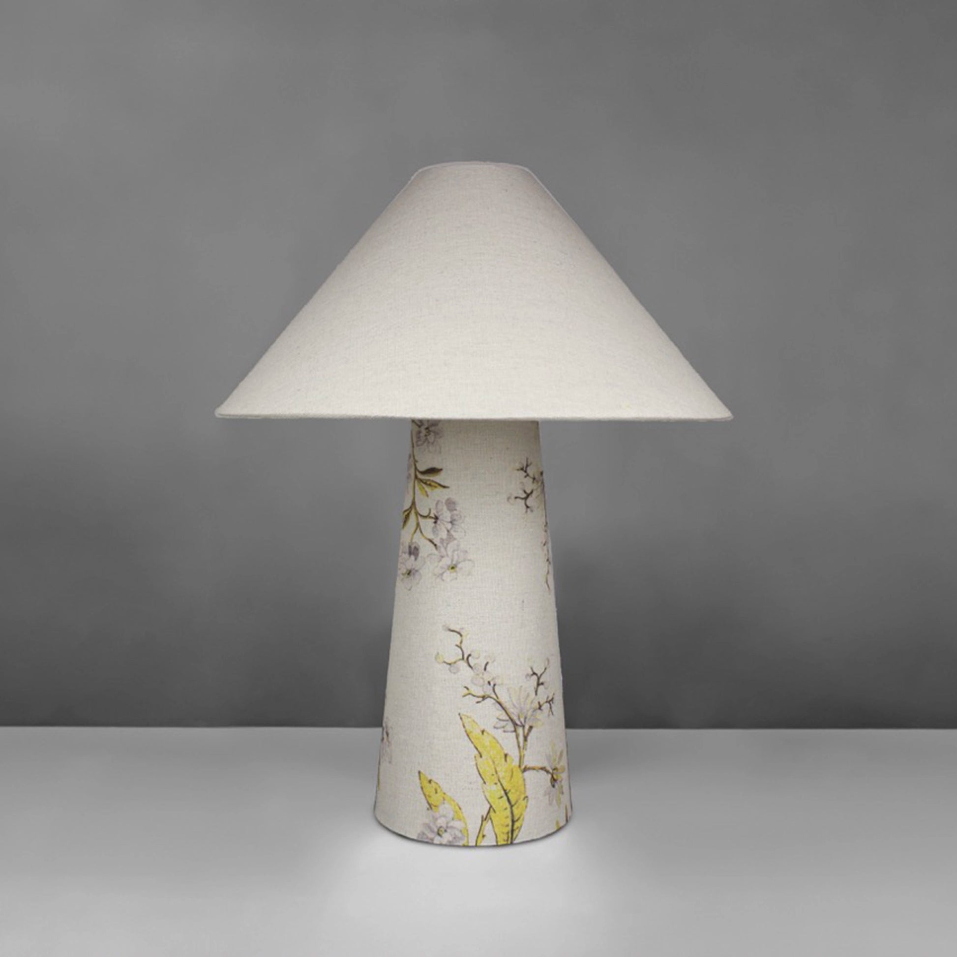 A fabric table lamp with shade and a yellow blossom design on the conical base