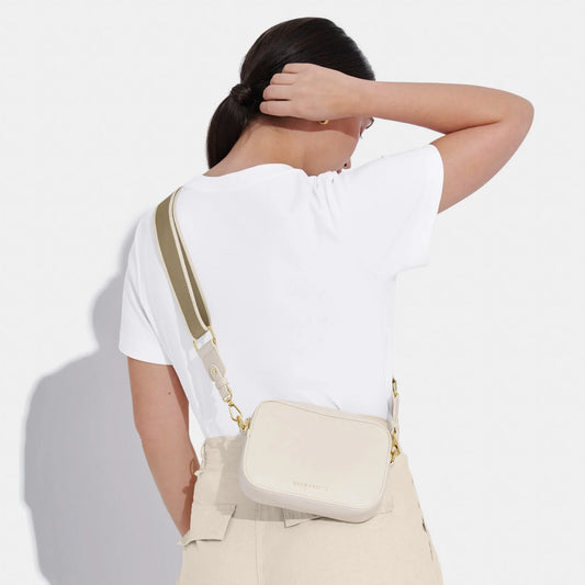 An off-white crossbody bag in a simple box shape with adjustable canvas strap and gold hardware on model