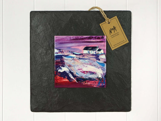 Wall art of a small white cottage in a field done in pinks and purples in an abstract style onto a square ceramic tile mounted on square slate