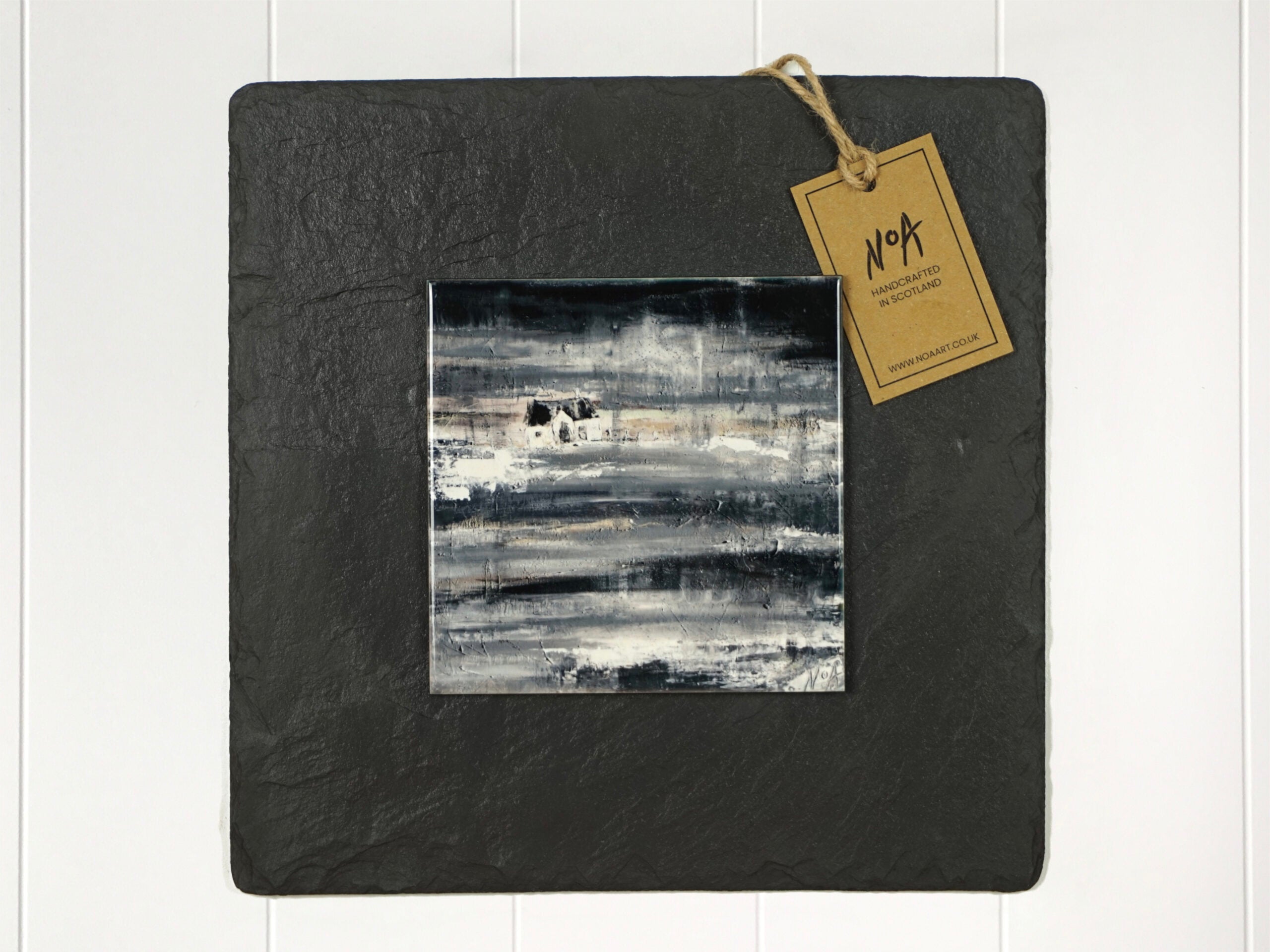 Wall art of a small white cottage on a rainy sleety day in grey done in an abstract style onto a square ceramic tile mounted on square slate