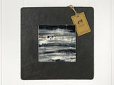 Wall art of a small white cottage on a rainy sleety day in grey done in an abstract style onto a square ceramic tile mounted on square slate